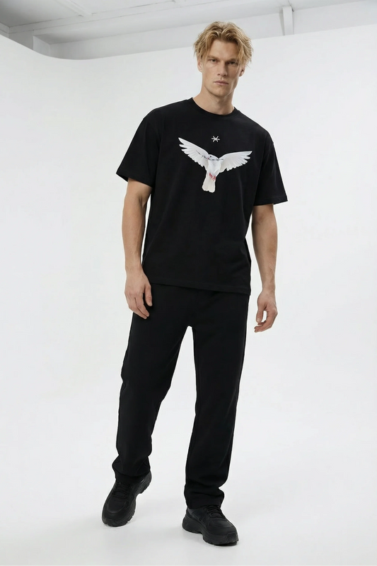 Man wearing a black t-shirt with a white dove and tiny 'Ominous' brand logo graphic design on a white background in a white photography studio