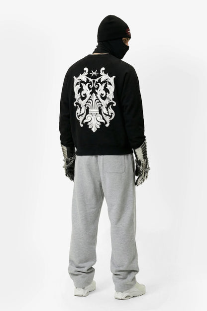 Person wearing a black hoodie with a white emblem on the back, gray pants, and white shoes on a white background.
