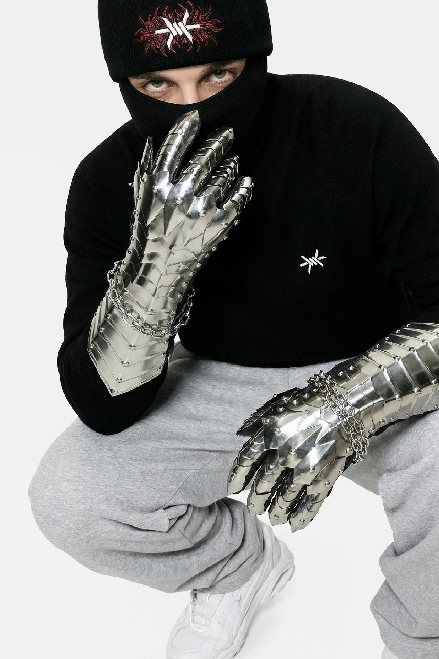 Person wearing metallic gloves and a black beanie with a logo on a white background
