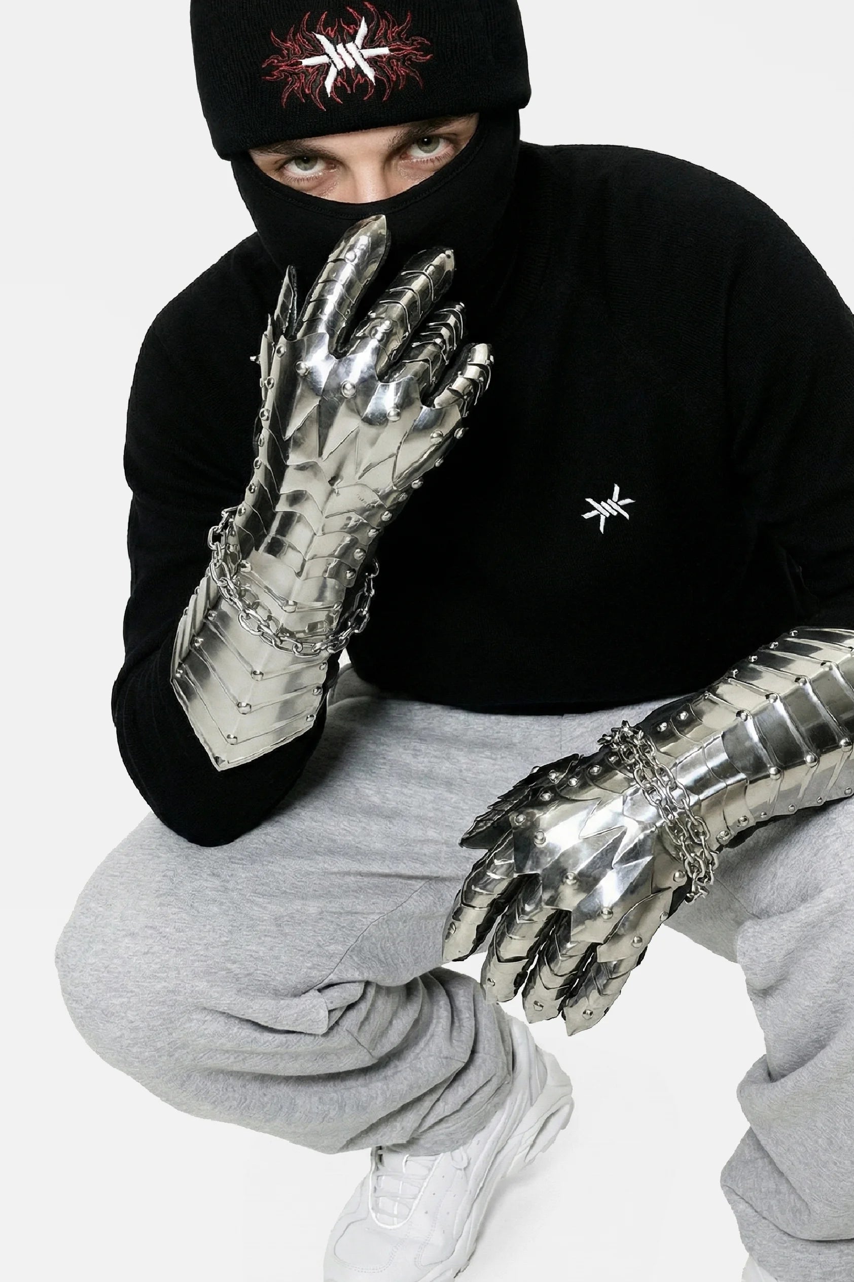 Person wearing metallic gloves and a black beanie with a logo on a white background