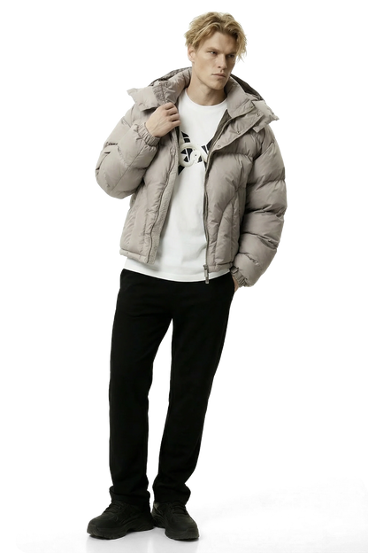Man wearing a beige gray puffer jacket over a white shirt with black pants on a white background