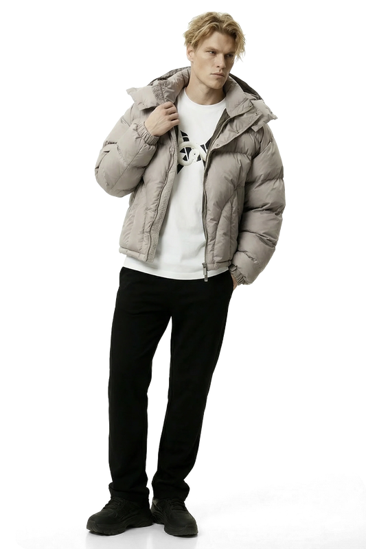 Man wearing a beige gray puffer jacket over a white shirt with black pants on a white background