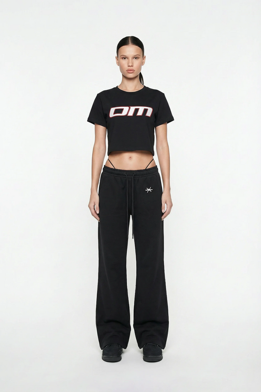 Woman wearing a black t-shirt with 'OM' logo and black pants on a white background