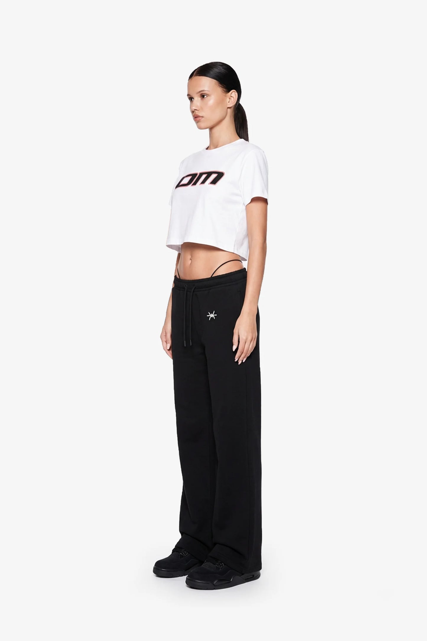 Ominous OM Cropped White Tee - Woman wearing a white crop top with a logo and black pants on a white background