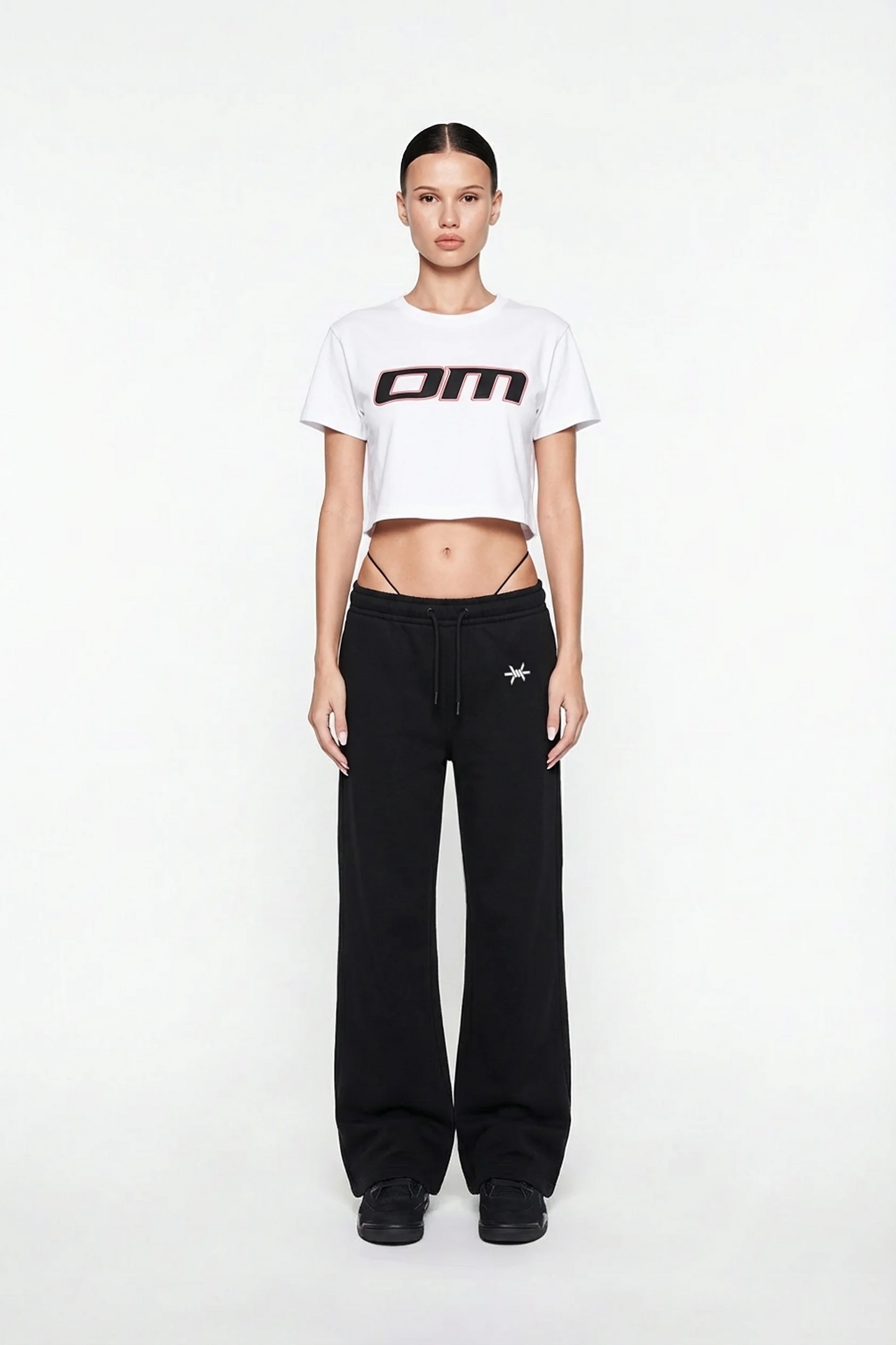 Ominous OM Cropped White Tee - Person wearing a white cropped t-shirt with a logo and black pants on a white background