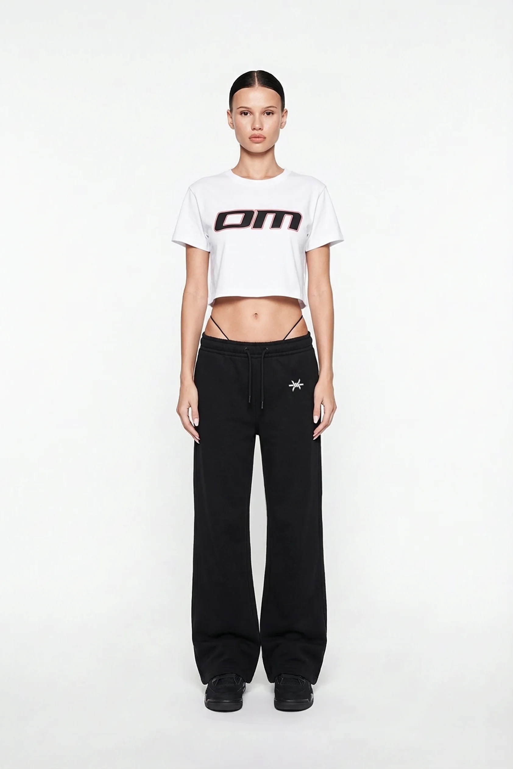 Ominous OM Cropped White Tee - Person wearing a white cropped t-shirt with a logo and black pants on a white background
