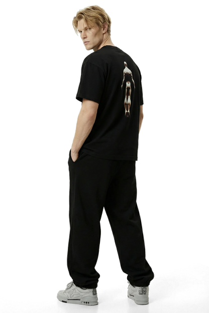 Ominous Ascendance Heavyweight Tee - Person wearing a black t-shirt with a graphic on the back and black pants on a white background