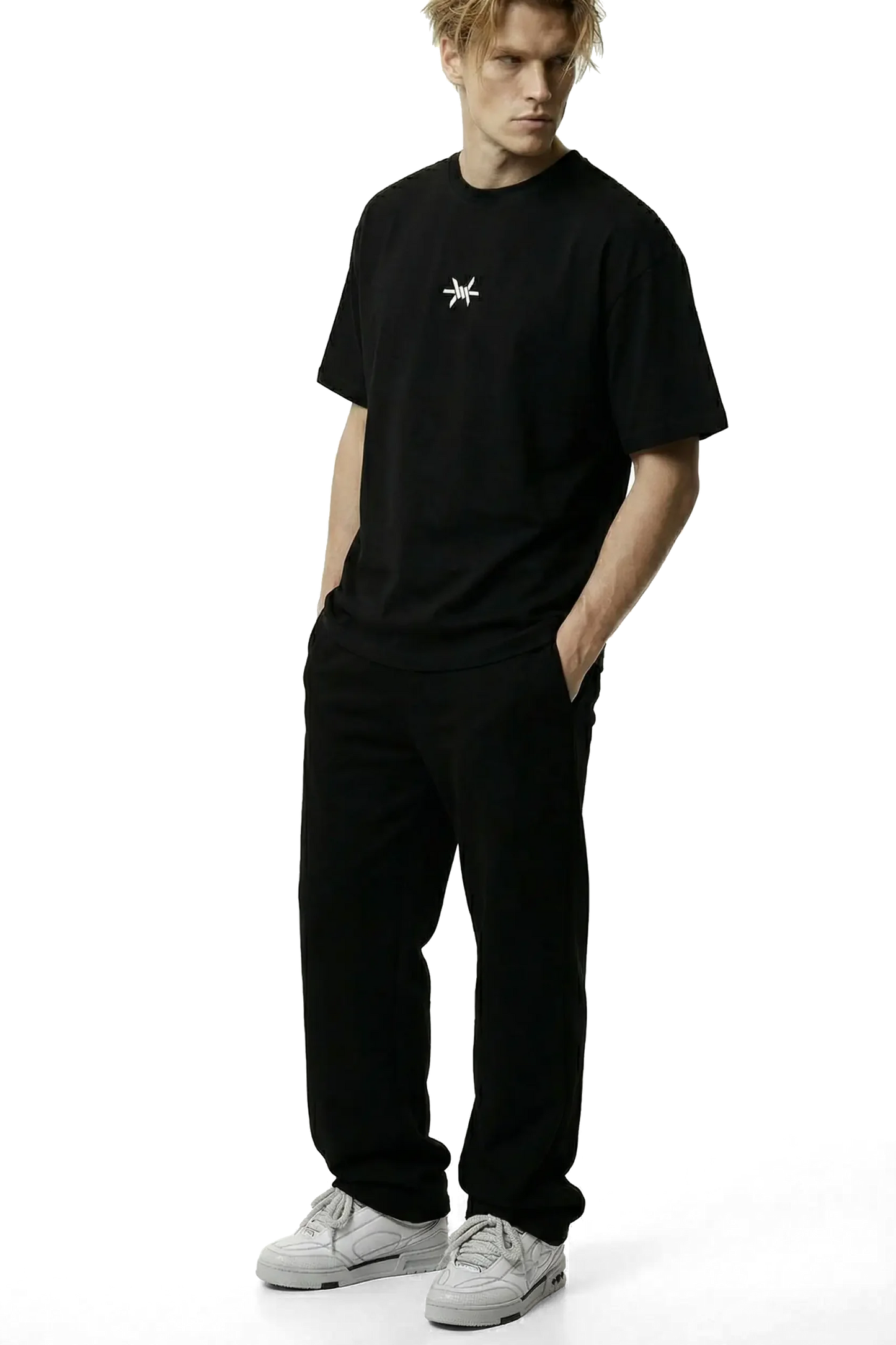 Ominous Ascendance Heavyweight Tee - Man wearing an oversized heavyweight black t-shirt with a small white 'Ominous' logo in the upper centre chest area and black pants on a white background