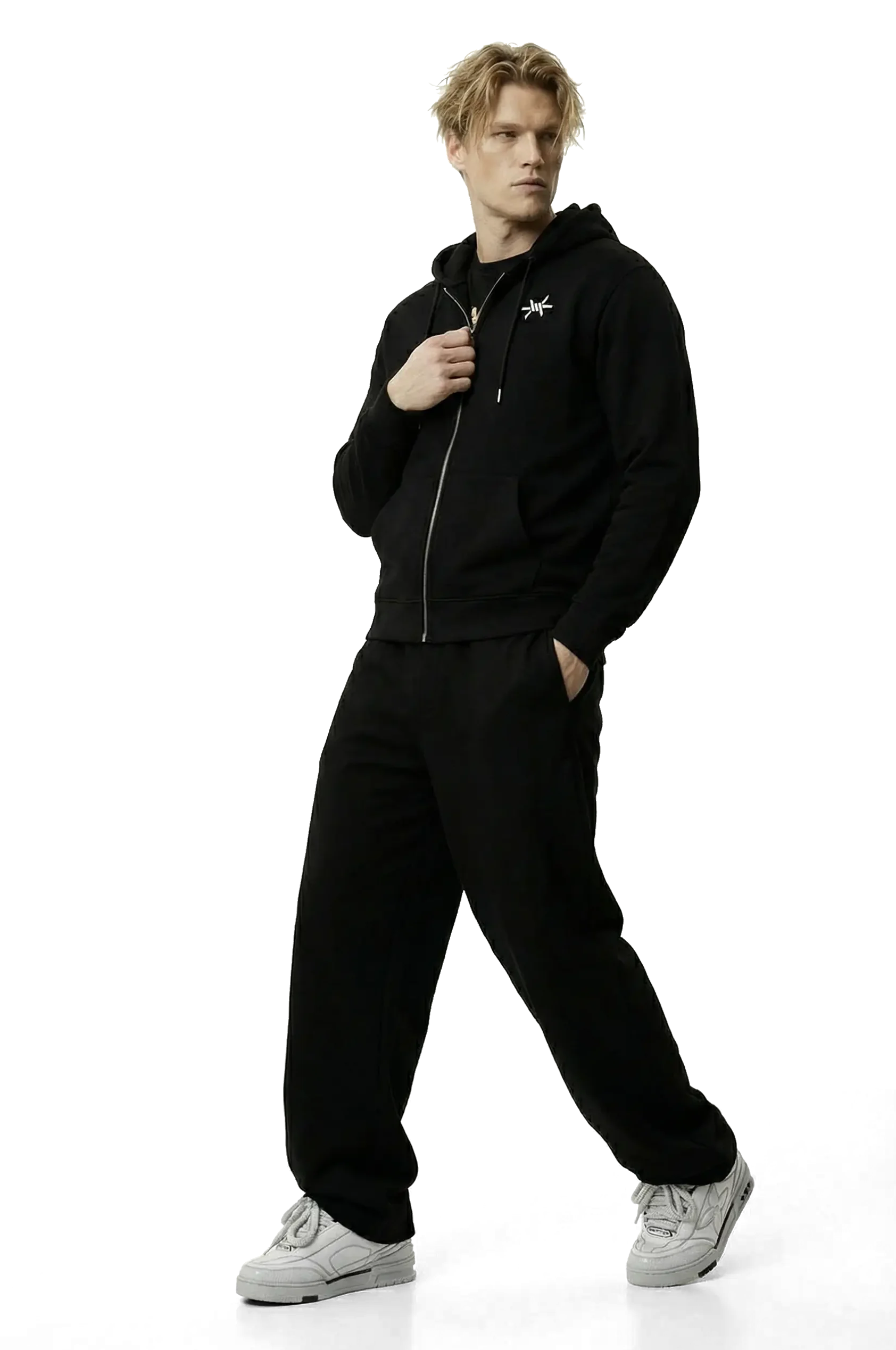 Man wearing a black zip up hoodie with a small logo and black trousers on a white background
