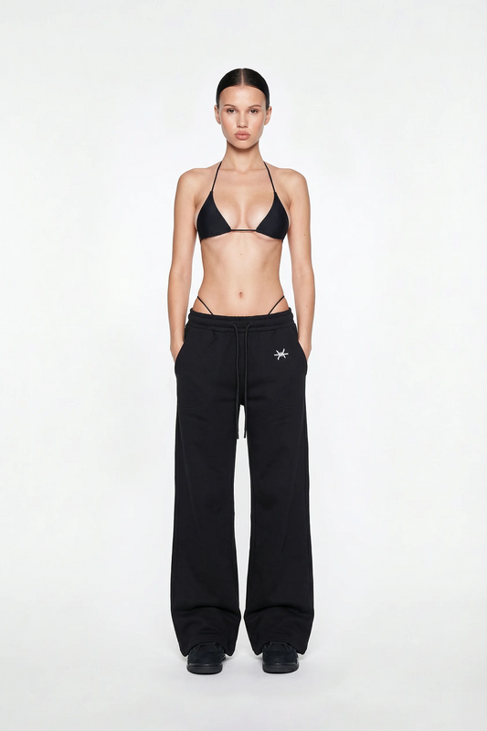 Model wearing black high-waisted pants with a small logo and a black bikini top on a white background.