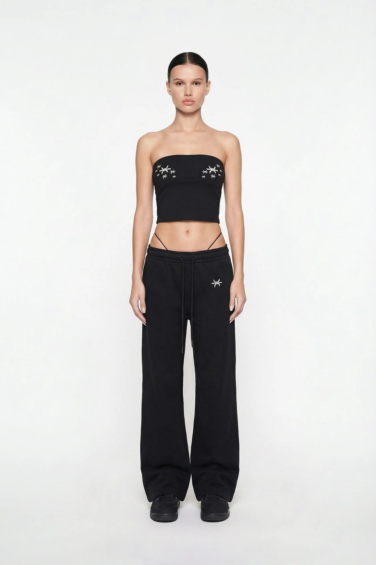 Person wearing a black strapless top and black pants with white logos on a white background