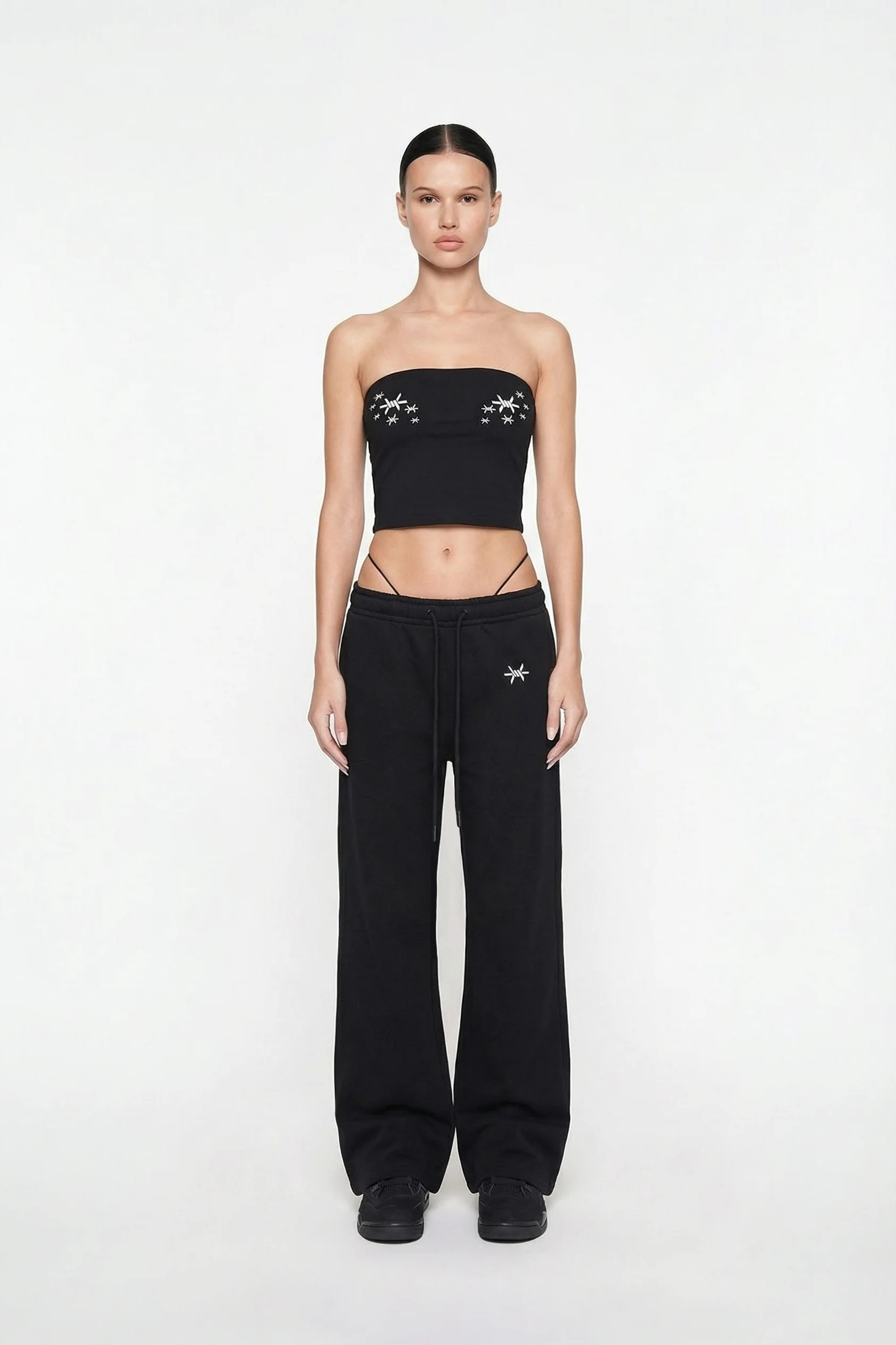 Person wearing a black strapless top and black pants with white logos on a white background