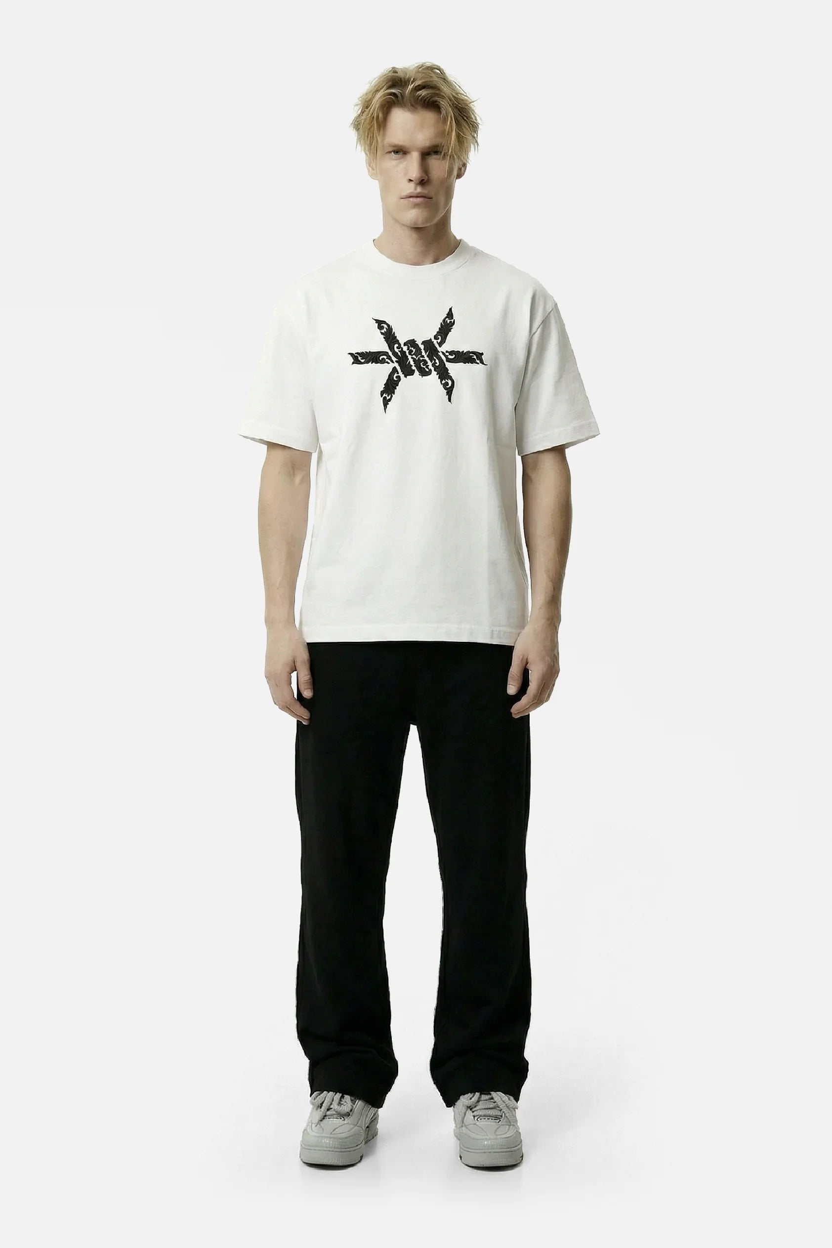 Man wearing a white t-shirt with a black baroque 'Ominous' brand logo graphic design on a white background