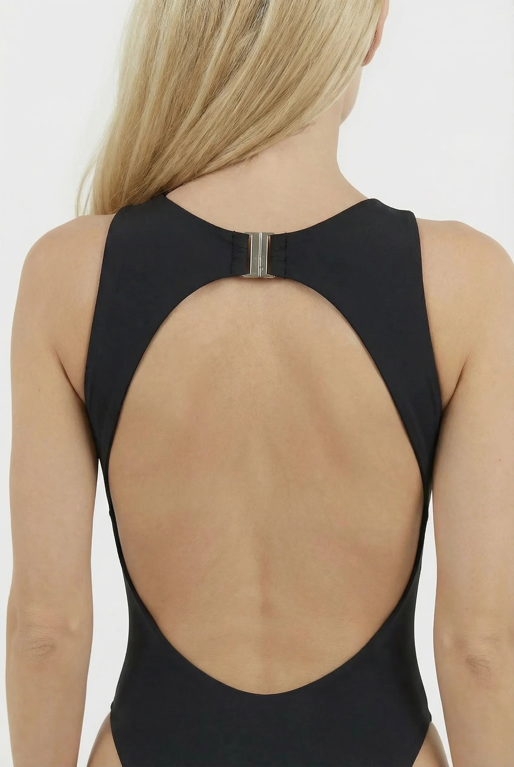 Woman wearing a black swimsuit with open back on a plain background